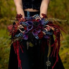 a woman wearing a black dress holding a purple and red flower bouquet in her hands