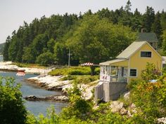 a small yellow house sitting on top of a lush green hillside next to the ocean