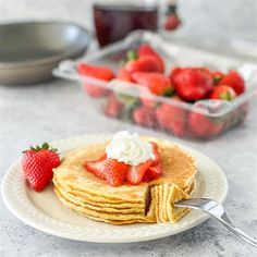 a stack of pancakes topped with whipped cream and strawberries on a plate next to a bowl of strawberries