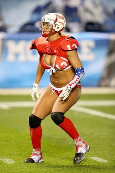 a female football player wearing red and white uniform on the field with her hands in her pockets