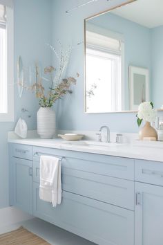 a bathroom with light blue walls and white counter tops, along with a large mirror above the sink