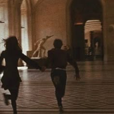 two people are running in the middle of a room with statues on either side of them