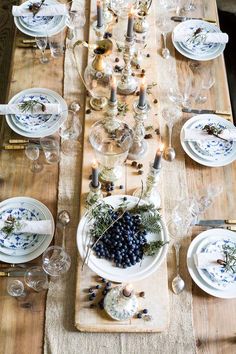 the table is set with white plates and silverware, blue berries, candles and greenery