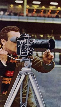 a man holding a camera up to his face while looking through the lens on a tripod