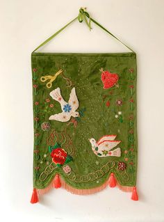 a green wall hanging with embroidered birds and flowers on it's sides, along with tassels