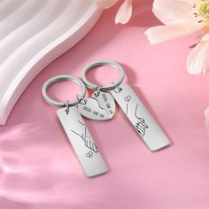 two silver key chains with engraved names on them and a pink flower in the background