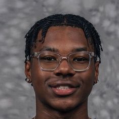 a man with glasses and a necklace on his neck posing for a photo in front of a gray background