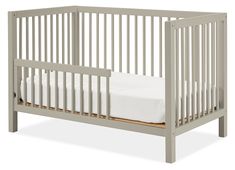 a baby crib with white sheets on the bottom and side rails, in grey