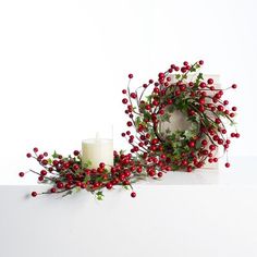 two candles are next to a wreath with red berries on it