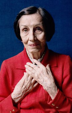 an older woman wearing a red jacket and holding her hands in front of her chest