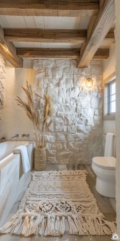 a bathroom with stone walls and flooring is pictured in this image, it has a rug on the floor