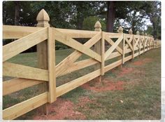 a wooden fence in the middle of a grassy area with trees and grass behind it