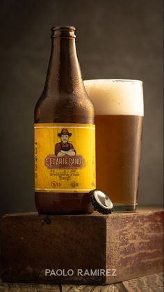 a bottle of beer sitting next to a glass on top of a wooden block with a lid