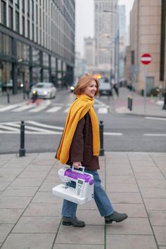 a woman is walking down the street carrying a purple and white cooler in her hand