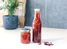 two jars filled with red liquid sitting on top of a table next to a potted plant