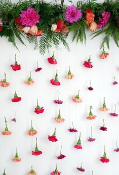 pink and red flowers hanging from the side of a white wall with greenery on it