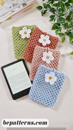 three crocheted pouches with flowers on them next to a tablet and plant