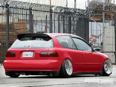 a red car is parked in front of a fence with bars on the top and bottom