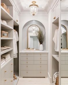 a walk - in closet with white cabinets and gold handles, an oval mirror on the wall