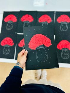 a person holding up a piece of paper with red designs on it in front of black and white squares