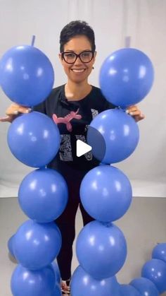 a woman standing in front of blue balloons with her hands on the top of them