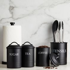 three black canisters with spoons and utensils in them on a marble countertop