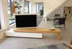 a flat screen tv sitting on top of a wooden table in a living room next to a stair case