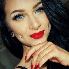 a woman with red lipstick and piercings posing for the camera while holding her hand on her chin