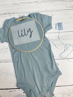 a baby bodysuit with the word july printed on it next to ear buds and wires