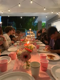 a group of people sitting around a table with plates and cups on it eating food