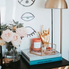 a table with flowers and a gold hand on it next to a vase filled with pink roses