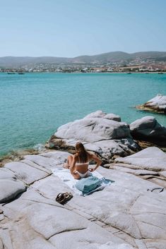 a woman is sitting on rocks by the water