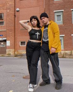 a man and woman standing next to each other in front of a tall brick building