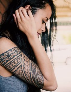 a woman with a tattoo on her arm holding her hand up to her face and looking down