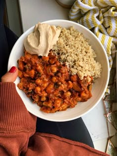 a white bowl filled with rice and beans next to a woman's red sweater