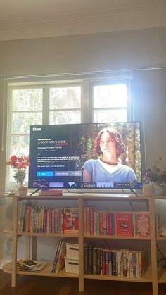 a television sitting on top of a wooden stand in front of a window with books