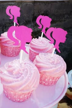 cupcakes with pink frosting are on a white cake plate and have pink decorations