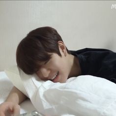 a young boy laying on top of a bed next to a white pillow and remote control