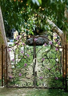 an iron gate with flowers on it in the middle of a lawn and surrounded by greenery