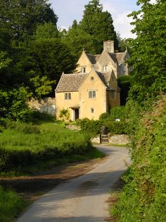 an old house is surrounded by lush green trees and bushes on the side of a road