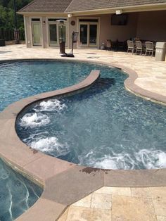 a large swimming pool with a waterfall in the middle and a patio area behind it