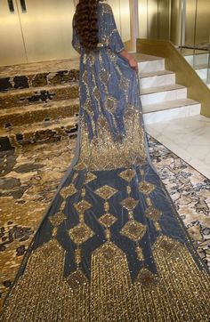 a woman standing in front of some stairs wearing a blue dress with gold sequins