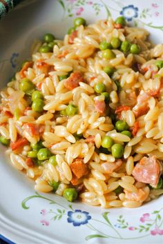 a plate full of pasta with peas and ham on it, next to a fork