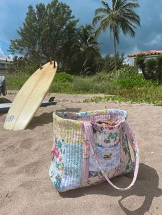 a tote bag sitting on top of a sandy beach next to a surfboard