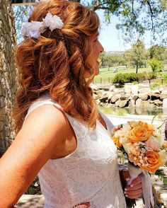 a woman holding a bouquet of flowers in her hand while standing next to a stone wall