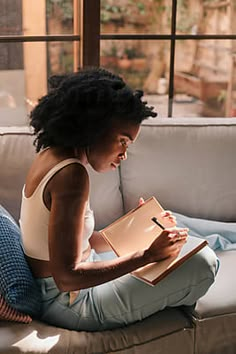 a woman sitting on a couch holding a binder and looking at a clipboard