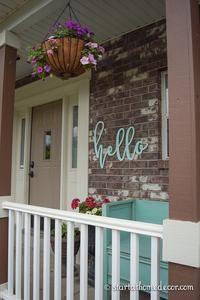 a welcome sign on the front porch of a house with flowers hanging from it's roof