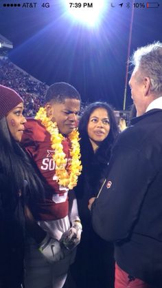 the football player is talking to two women and a man in a black suit at a game