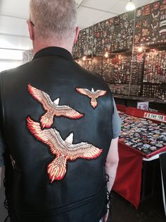 a man wearing a black leather vest with red and white birds embroidered on the back