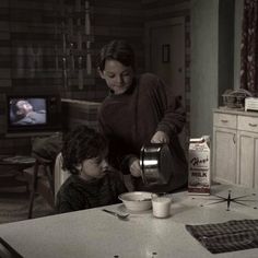 a woman pours milk from a pitcher to a little boy sitting at a table